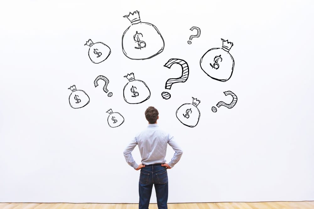 Pessoa pensativa analisando diversas ilustrações de sacolas de dinheiro e pontos de interrogação em uma parede branca, representando dúvidas financeiras.