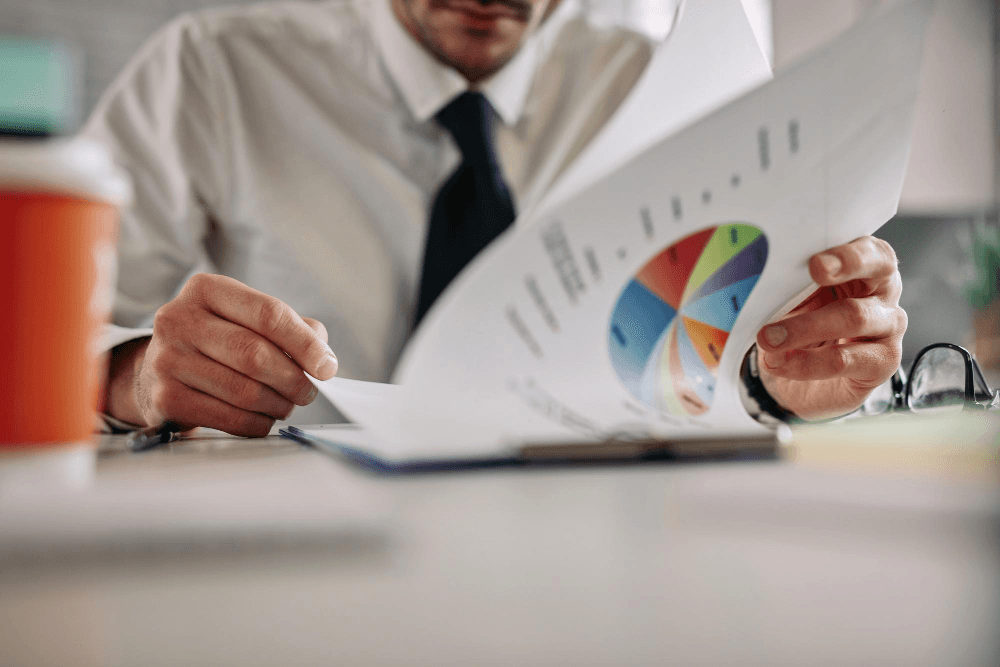 Homem de terno analisando gráficos e relatórios financeiros em um escritório moderno.
