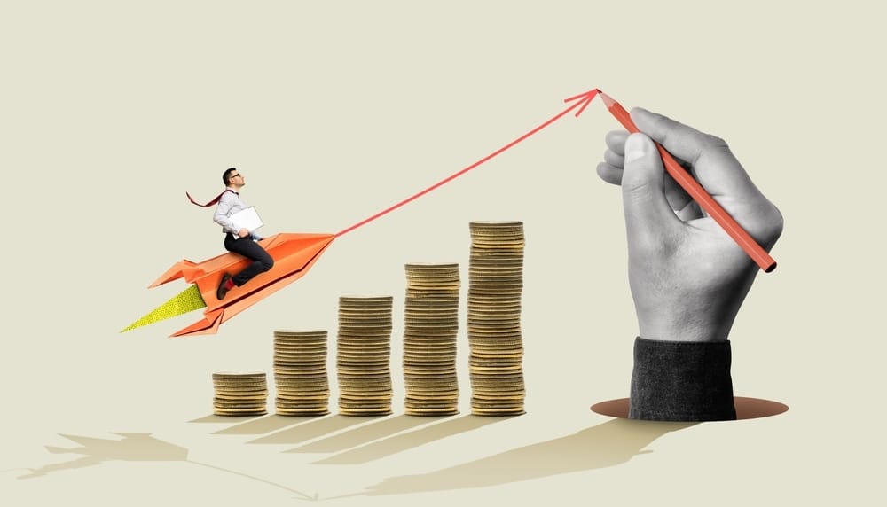 Uma representação visual de crescimento financeiro, onde um homem em um foguete de papel alaranjado voa sobre pilhas crescentes de moedas, e uma mão desenha uma seta ascendente. A imagem simboliza a escalada do lucro após a correta identificação de o que é custo fixo para planejar o investimento.