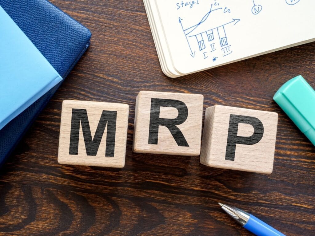Imagem com blocos de madeira exibindo as letras M, R e P, em um ambiente de escritório com uma agenda, canetas e papel com anotações e gráficos.