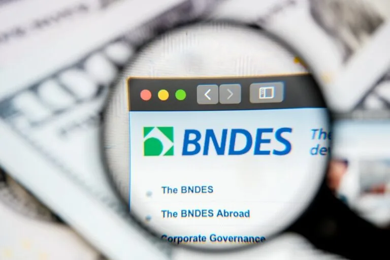 Imagem de uma lupa focada na tela de um computador com o logo do BNDES destacando-se na pesquisa online.
