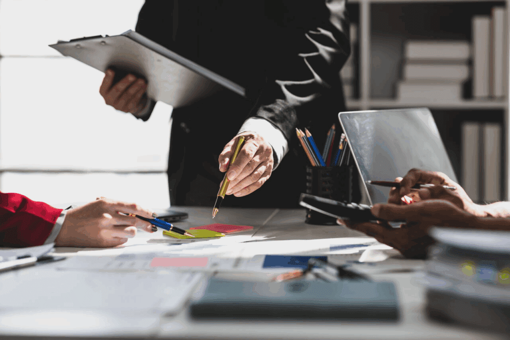 Executivos analisando relatórios financeiros sobre a mesa, com apontamentos e uso de calculadora durante reunião de gestão de custos