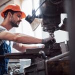 Trabalhador operando máquina industrial, representando um exemplo de custos diretos ligados à mão de obra e produção.